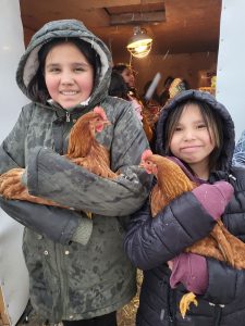 two girls smile posting with chickens