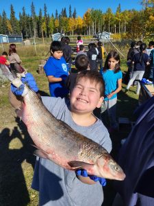 a group of kids pose for the camera, with a little boy in front posing with a fish