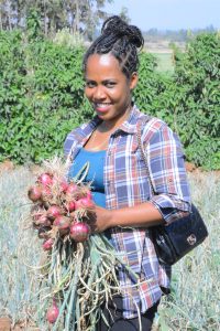a woman smiles, holding a freshly picked bunch of onion